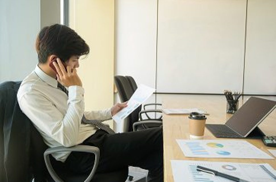 Young executives are calling to check the organization's performance reports.He looked at the data graph in hand, graphs, laptop, coffee on the desk in the office.